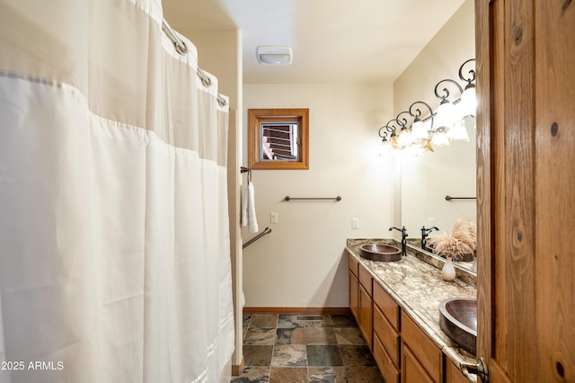 bathroom with double vanity, baseboards, stone finish floor, and a sink