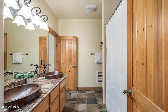 bathroom with stone finish flooring, a sink, baseboards, and double vanity