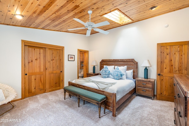 bedroom featuring wooden ceiling, a skylight, a ceiling fan, and light colored carpet