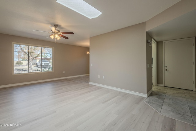 spare room featuring a skylight, light hardwood / wood-style flooring, and ceiling fan