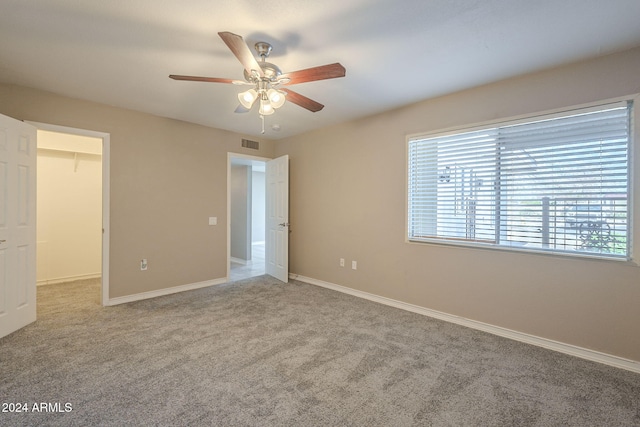 unfurnished bedroom featuring a closet, a walk in closet, light colored carpet, and ceiling fan