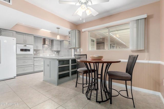 kitchen with white appliances, tasteful backsplash, hanging light fixtures, gray cabinetry, and wall chimney range hood