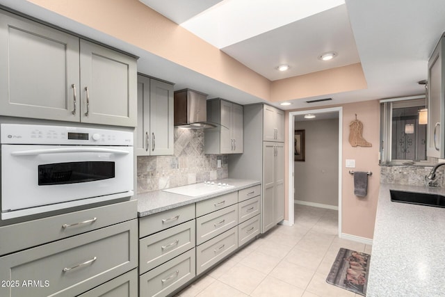 kitchen featuring white appliances, wall chimney exhaust hood, sink, backsplash, and light tile patterned floors