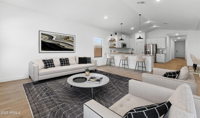living room featuring light wood-style floors, visible vents, baseboards, and lofted ceiling