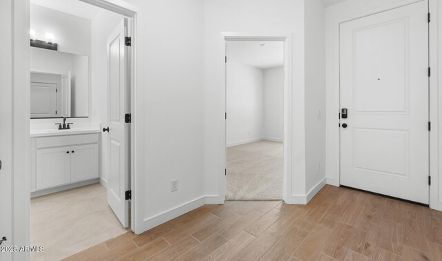 hallway featuring a sink, baseboards, and light wood-type flooring