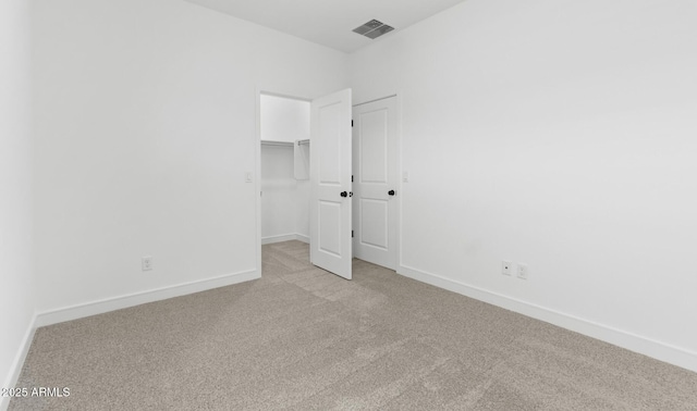 unfurnished bedroom featuring a walk in closet, light carpet, baseboards, and visible vents