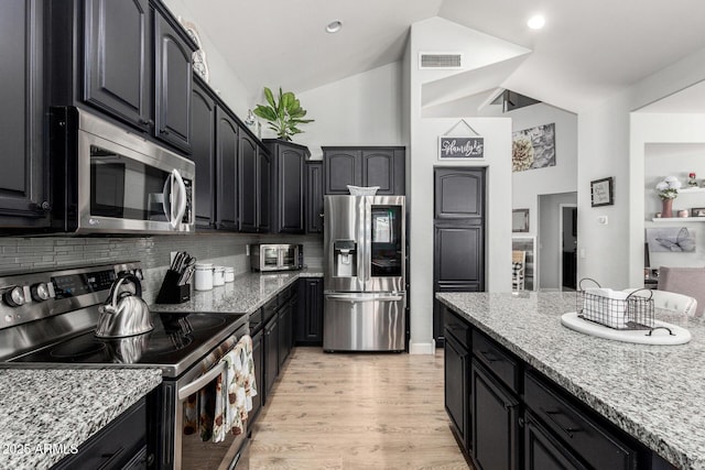 3545 W Tanner Ranch Rd, San Tan Valley, AZ 85144 - kitchen with appliances with stainless steel finishes, vaulted ceiling, dark cabinetry, backsplash, and light stone counters