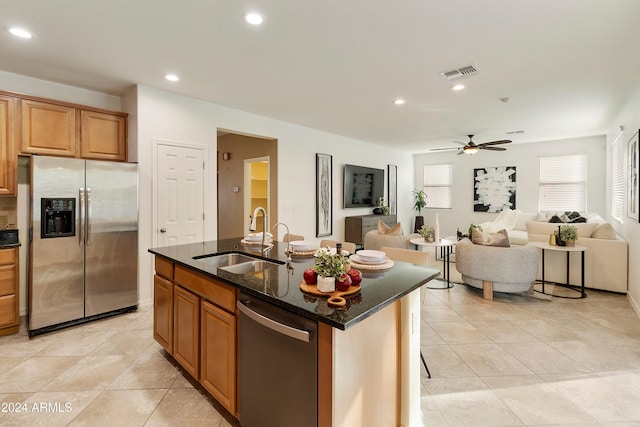 kitchen featuring ceiling fan, appliances with stainless steel finishes, an island with sink, dark stone countertops, and sink