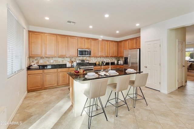 kitchen featuring a breakfast bar area, backsplash, an island with sink, sink, and stainless steel appliances