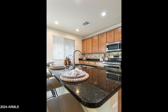 kitchen with sink, a kitchen bar, backsplash, stainless steel appliances, and dark stone counters