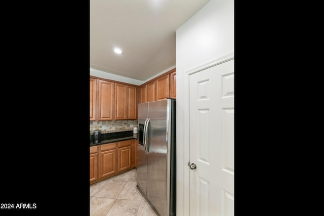 kitchen with stainless steel fridge, light tile patterned flooring, dark stone counters, and tasteful backsplash