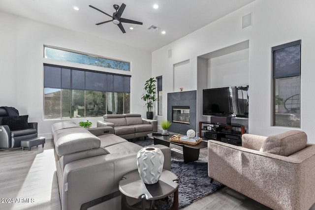 living room with a towering ceiling, light hardwood / wood-style flooring, ceiling fan, and a tiled fireplace