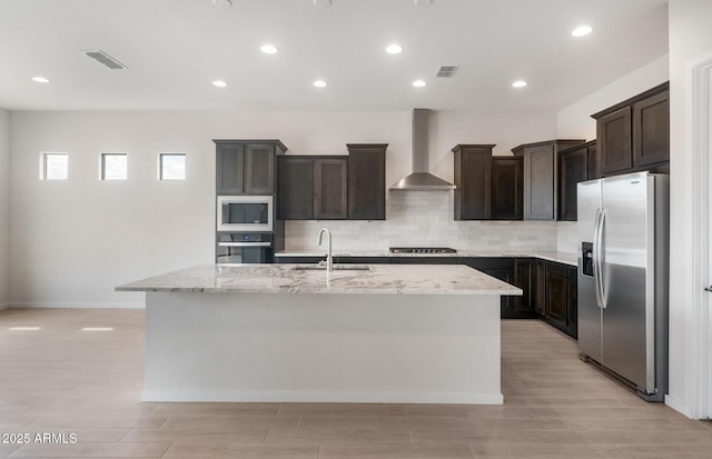 22523 E Orchard Ln, Queen Creek, AZ 85142 - kitchen with stainless steel appliances, wall chimney range hood, a sink, a kitchen island with sink, and light stone countertops
