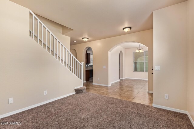 empty room with light colored carpet and a notable chandelier