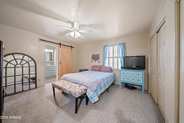 carpeted bedroom with a barn door, a textured ceiling, ceiling fan, and ensuite bathroom