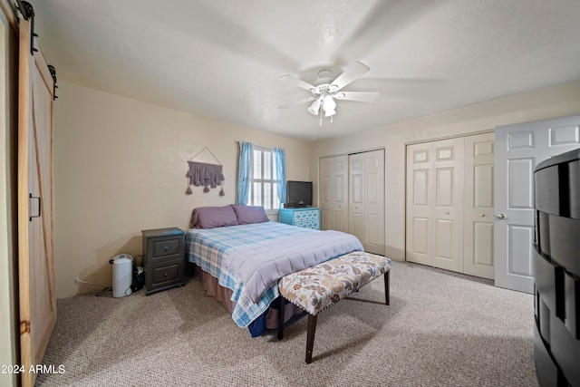 bedroom with light carpet, multiple closets, ceiling fan, and a barn door