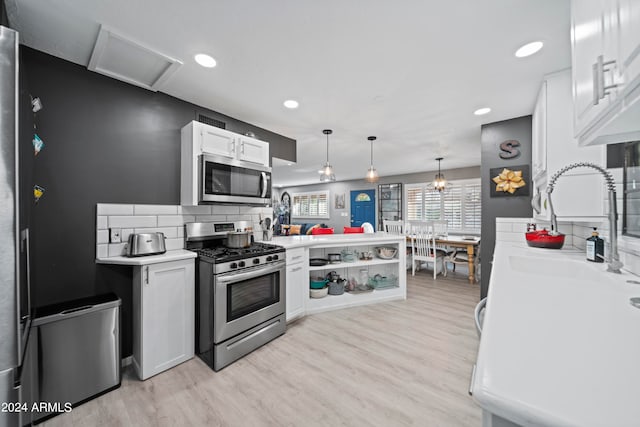 kitchen featuring pendant lighting, kitchen peninsula, white cabinetry, appliances with stainless steel finishes, and light hardwood / wood-style floors