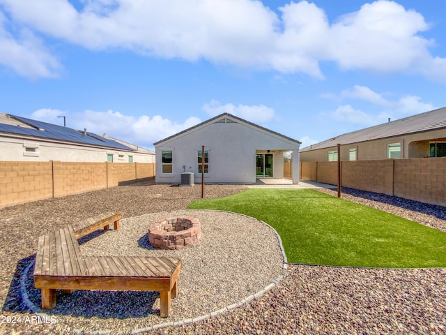 back of property with stucco siding, a lawn, central AC unit, a fenced backyard, and a fire pit