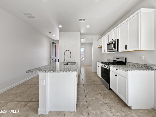 kitchen with a kitchen island with sink, stainless steel appliances, light stone counters, sink, and white cabinets