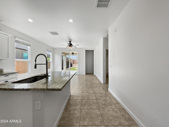 kitchen featuring light tile patterned floors, a sink, visible vents, baseboards, and dark stone countertops