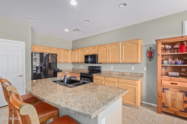 kitchen with a center island with sink, sink, black appliances, and a kitchen breakfast bar