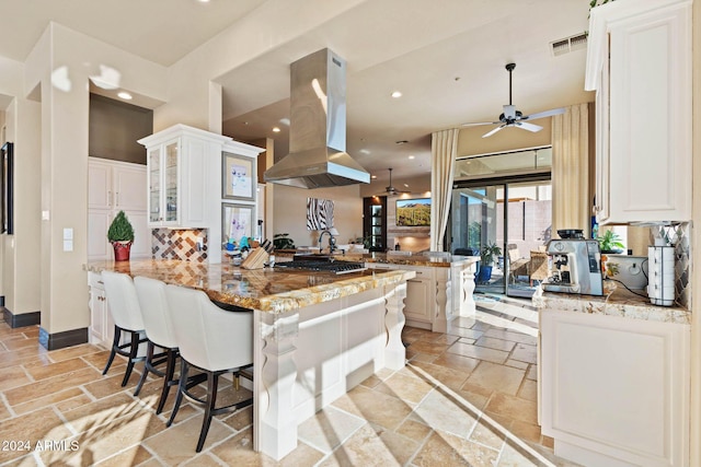 2549 W Shinnecock Way, Anthem, AZ 85086 - kitchen featuring island exhaust hood, a peninsula, stone tile floors, a ceiling fan, and tasteful backsplash
