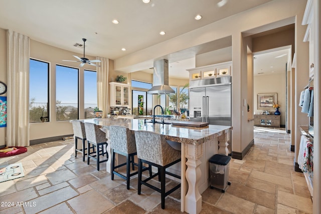 kitchen featuring island exhaust hood, a large island, a healthy amount of sunlight, and light stone counters