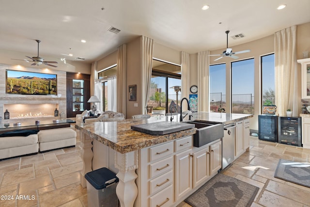 kitchen featuring light stone counters, sink, a center island with sink, dishwasher, and wine cooler