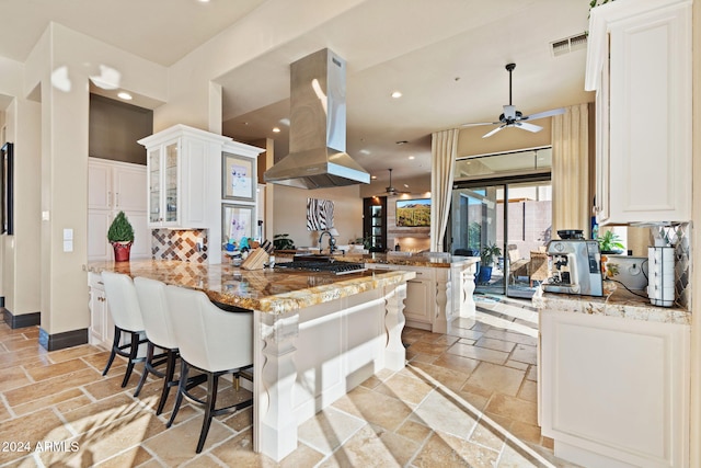 kitchen featuring light stone countertops, kitchen peninsula, island exhaust hood, a breakfast bar, and white cabinets