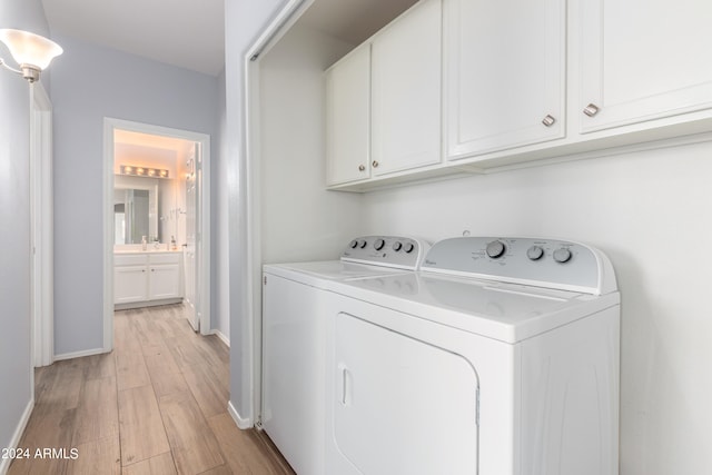 clothes washing area featuring washing machine and dryer, light wood-type flooring, and cabinets