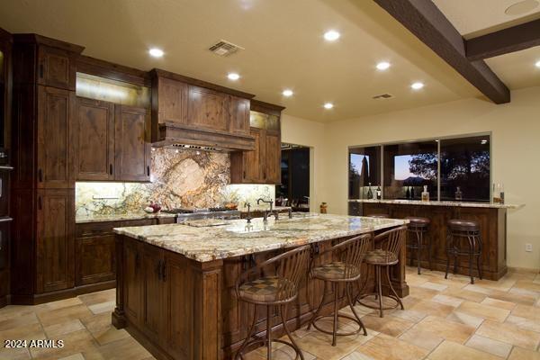 kitchen with beamed ceiling, light stone countertops, a breakfast bar area, backsplash, and a large island