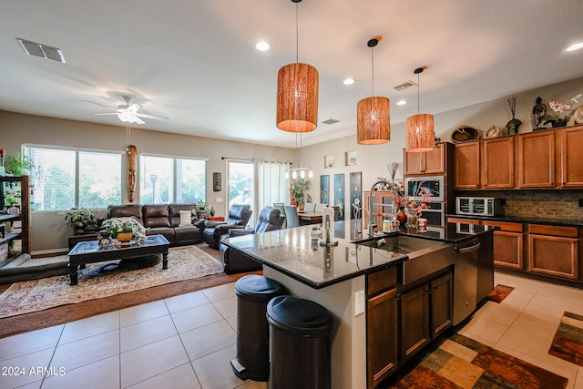 kitchen featuring ceiling fan, pendant lighting, light tile patterned flooring, a center island with sink, and decorative backsplash