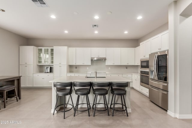 kitchen featuring stainless steel appliances, an island with sink, decorative backsplash, and white cabinets