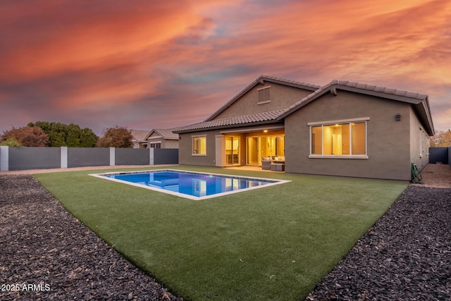 back house at dusk with a fenced in pool, an outdoor living space, and a yard