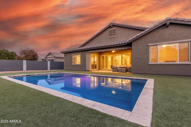 pool at dusk with outdoor lounge area and a lawn