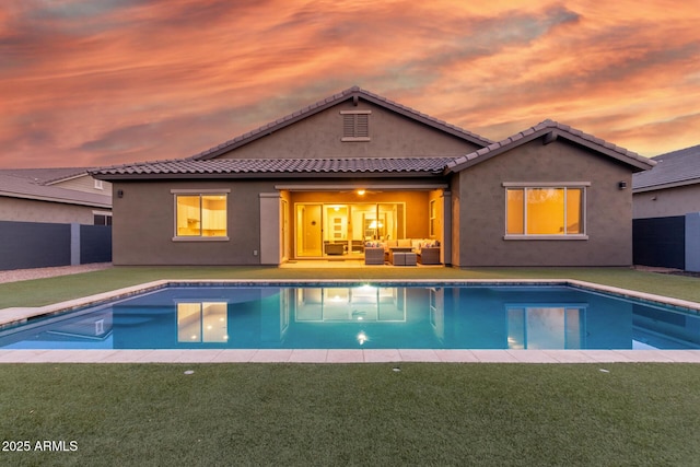 pool at dusk with outdoor lounge area and a lawn