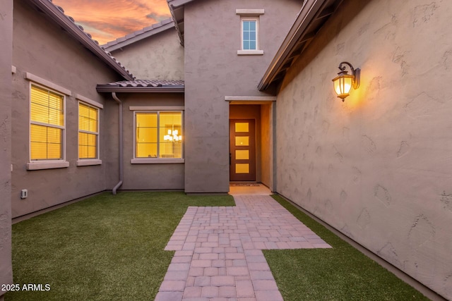 exterior entry at dusk featuring a yard and a patio area