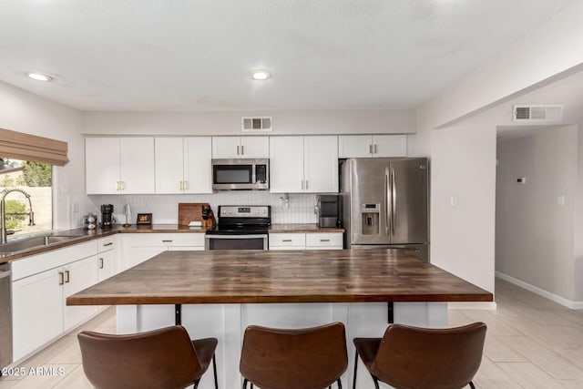 kitchen featuring appliances with stainless steel finishes, sink, white cabinets, tasteful backsplash, and butcher block counters