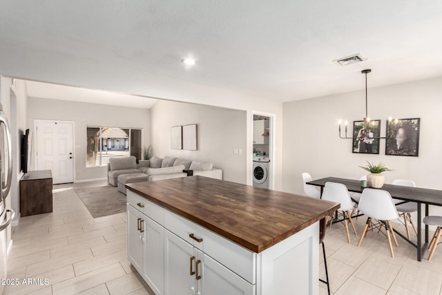 kitchen with butcher block counters, white cabinetry, hanging light fixtures, washer / dryer, and a kitchen island