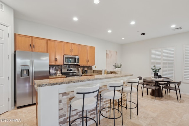 11299 E Greythorn Dr, Scottsdale, AZ 85262 - kitchen with appliances with stainless steel finishes, recessed lighting, a kitchen breakfast bar, decorative backsplash, and light stone counters
