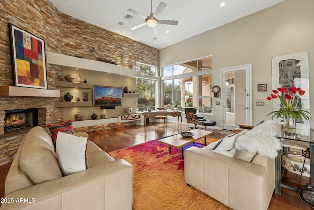 living room featuring a fireplace, wood finished floors, a ceiling fan, and a towering ceiling