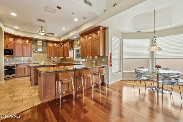 kitchen with brown cabinets, wall chimney exhaust hood, visible vents, and stainless steel appliances