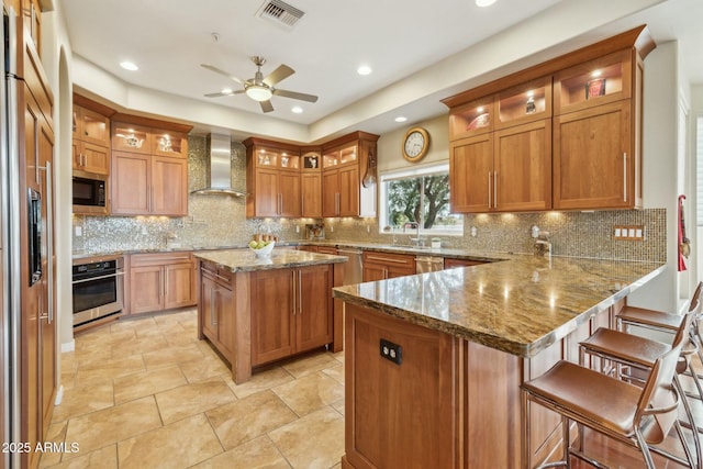 kitchen with wall chimney exhaust hood, visible vents, built in appliances, and brown cabinets