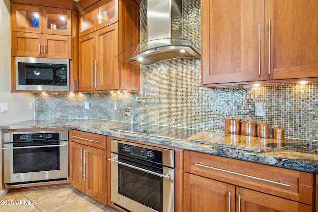 kitchen with wall chimney exhaust hood, light stone countertops, light tile patterned flooring, and stainless steel appliances