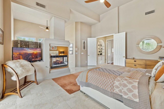 bedroom featuring visible vents, a towering ceiling, and a multi sided fireplace