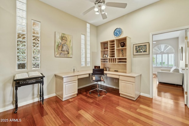 home office with baseboards, a ceiling fan, built in desk, and light wood-type flooring