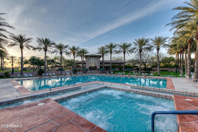 pool at dusk featuring a community pool, fence, a hot tub, and a patio area