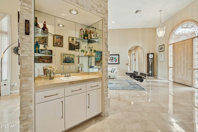 bathroom featuring visible vents, marble finish floor, baseboards, a towering ceiling, and vanity