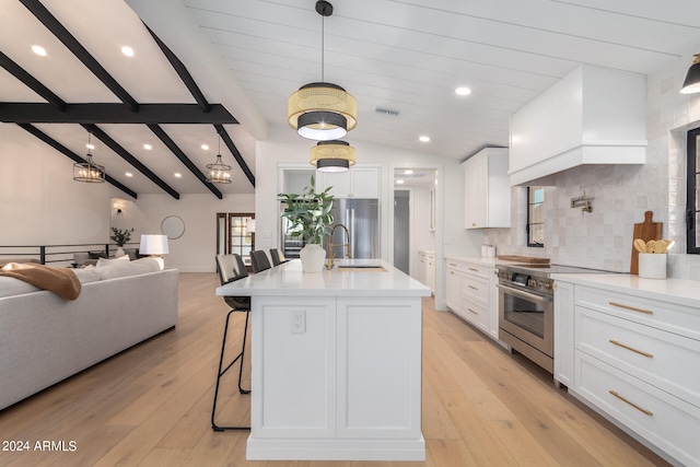 kitchen featuring vaulted ceiling with beams, a center island with sink, white cabinetry, appliances with stainless steel finishes, and light wood-type flooring