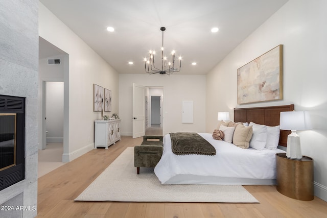 bedroom with a notable chandelier, a fireplace, and light hardwood / wood-style flooring